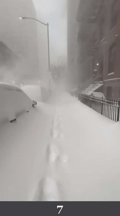 Schneebedeckte Straße mit einzelner Fußspur in Richtung Innenstadt. Beschreibung: Eine zentrale Spur führt durch tiefen Schnee entlang einer geraden Straßenachse, Gebäude rahmen die Szene symmetrisch ein. Könnte das real sein? Nein. Die Spur verläuft geometrisch mittig und die Schneestruktur ist homogen modelliert, ohne zufällige Verdichtungen oder Schmutzränder.