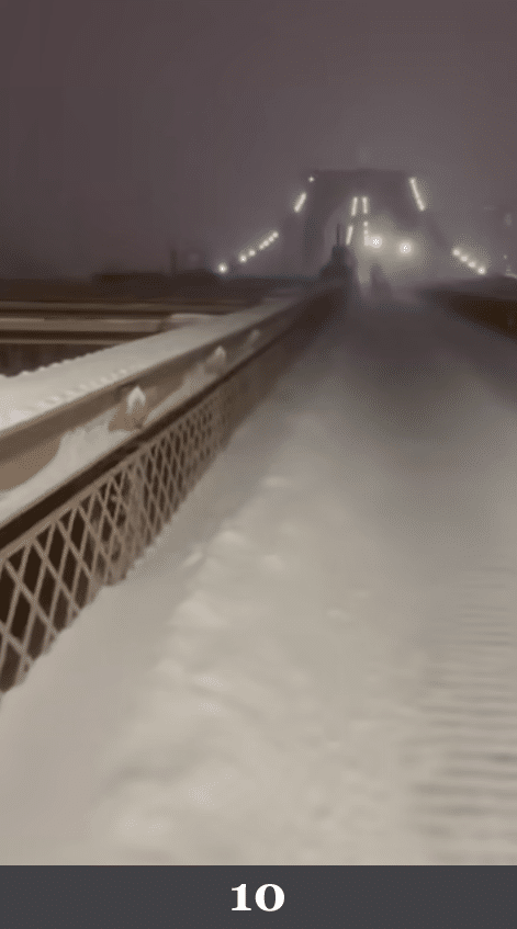 Verschneite Brücke mit gleichmäßig bedeckter Fahrbahn und Geländer. Beschreibung: Eine Brückenkonstruktion zieht sich in zentraler Perspektive in die Ferne, die Schneeschicht liegt homogen über der gesamten Oberfläche. Könnte das real sein? Nein. Die Schneedecke wirkt wie ein einheitlicher Mantel ohne Verdichtungen, Schmelzränder oder unregelmäßige Anlagerungen an Kanten.
